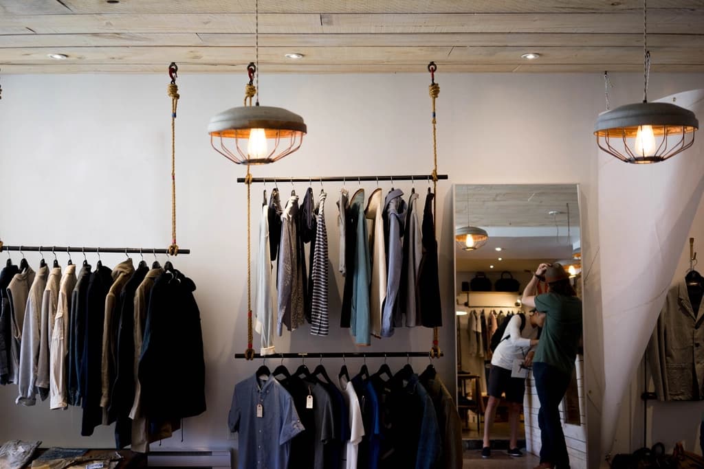 A bright clothing boutique with garments on hanging rails and pendant lamps