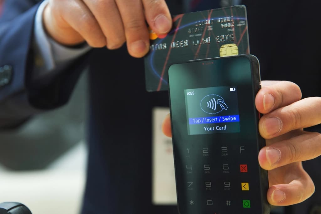 A customer holding a card above a handheld payment terminal showing a tap prompt