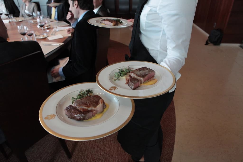 A server carrying two plated steak dishes in a restaurant