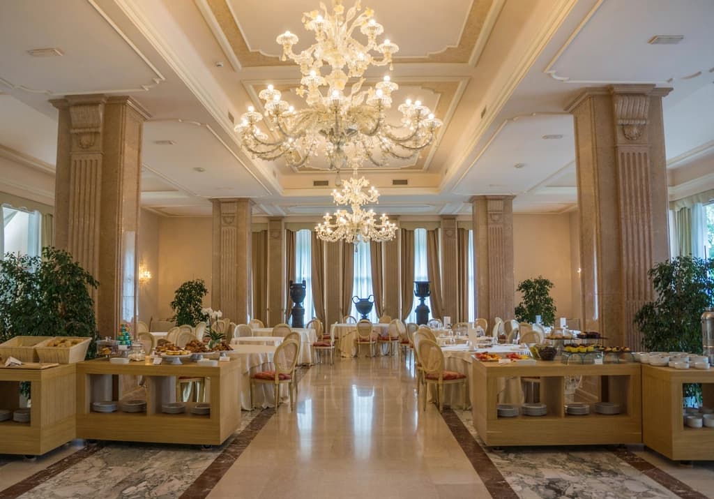 A large hotel dining hall with chandeliers and set tables